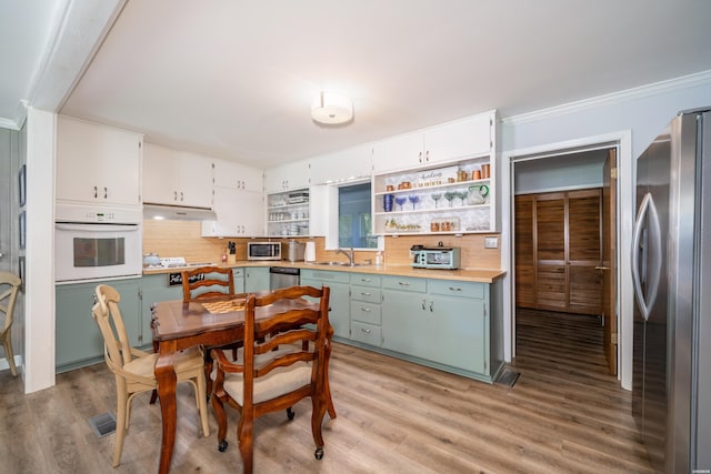 kitchen with a sink, stainless steel appliances, decorative backsplash, open shelves, and light wood-style flooring