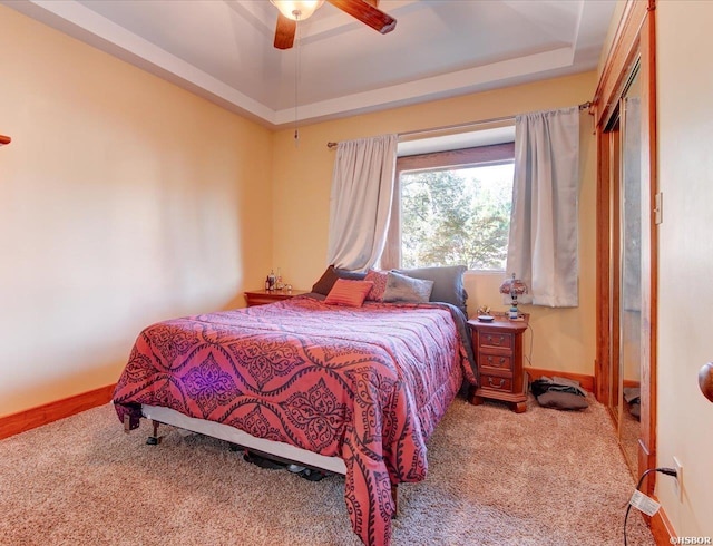 carpeted bedroom with a raised ceiling, a ceiling fan, and baseboards