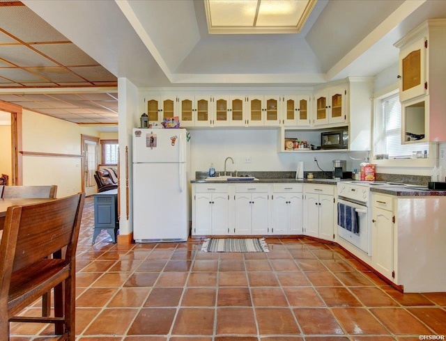 kitchen featuring white appliances, dark countertops, glass insert cabinets, a sink, and light tile patterned flooring