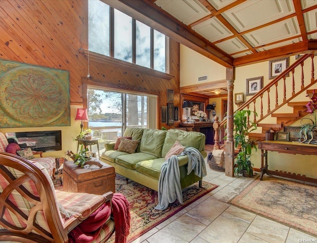 living area featuring a water view, visible vents, a glass covered fireplace, wood walls, and stairs