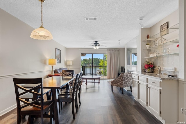 dining room with a textured ceiling, dark wood finished floors, visible vents, and a ceiling fan