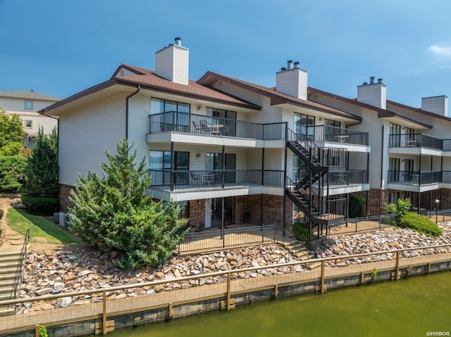 back of property with a chimney, brick siding, stairway, and a water view