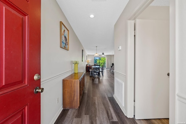 hallway featuring visible vents, dark wood finished floors, and a textured ceiling