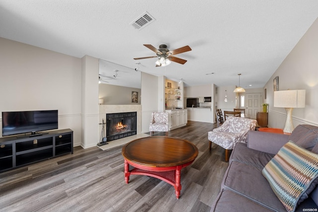 living area with a tile fireplace, visible vents, a textured ceiling, and wood finished floors