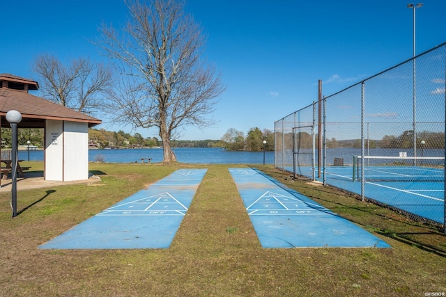 view of community with a water view, a tennis court, fence, and shuffleboard