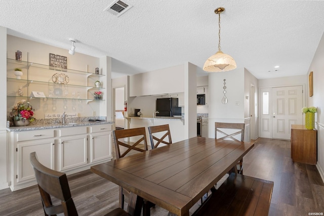 dining space featuring a textured ceiling, indoor wet bar, dark wood finished floors, and visible vents