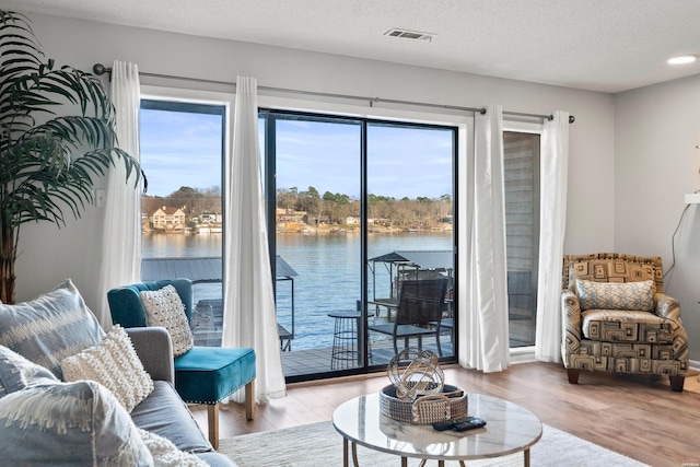 living area with visible vents, a textured ceiling, a water view, and wood finished floors