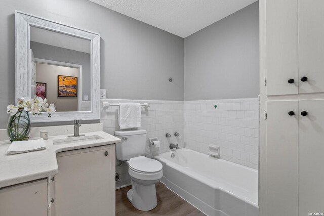 full bath with a textured ceiling, toilet, wood finished floors, vanity, and a bath