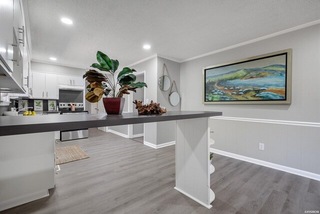 kitchen with a textured ceiling, a peninsula, white cabinets, stainless steel electric range oven, and a kitchen bar