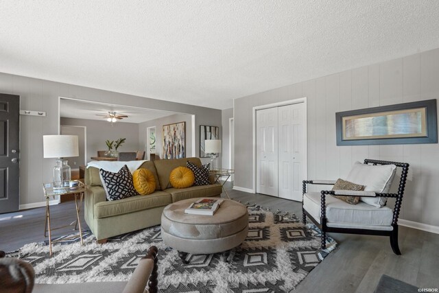 living room featuring dark wood-style floors, a ceiling fan, baseboards, and a textured ceiling