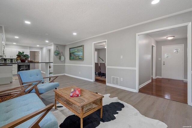 living area featuring a textured ceiling, wine cooler, wood finished floors, visible vents, and ornamental molding