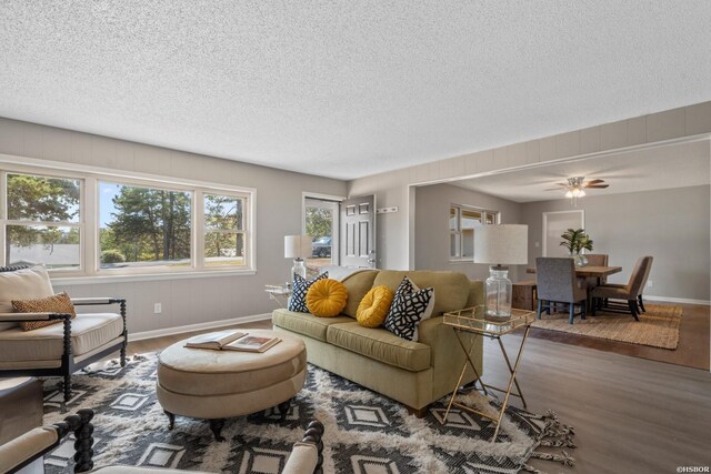 living room with a textured ceiling, ceiling fan, wood finished floors, and baseboards