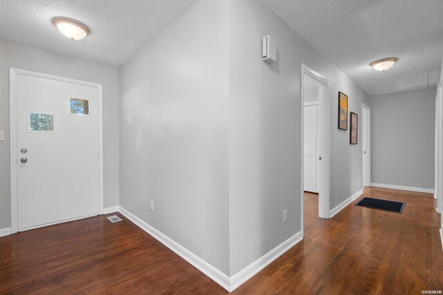 foyer with dark wood finished floors, a textured ceiling, and baseboards