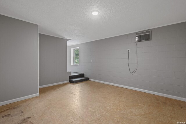 unfurnished room featuring concrete block wall, light floors, a textured ceiling, a wall mounted air conditioner, and baseboards