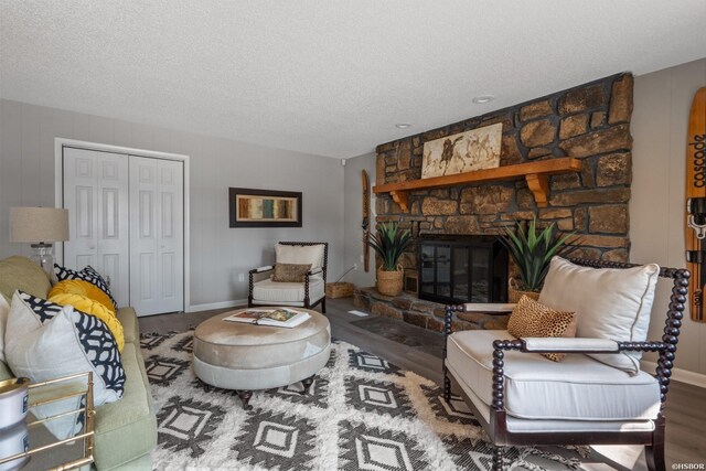 living room with a textured ceiling, a stone fireplace, wood finished floors, and baseboards