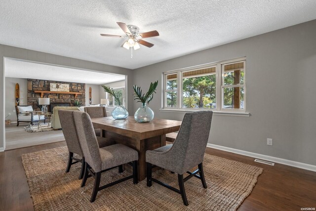 dining area featuring a textured ceiling, a stone fireplace, wood finished floors, visible vents, and baseboards