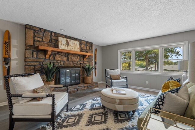 living area with a textured ceiling, wood finished floors, and a stone fireplace