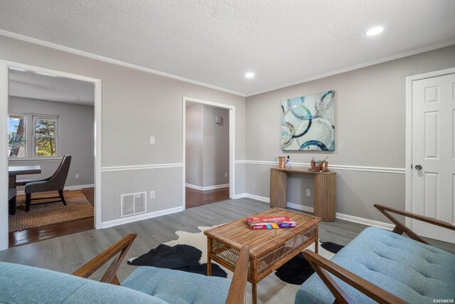 living area featuring a textured ceiling, dark wood-style flooring, wainscoting, and visible vents