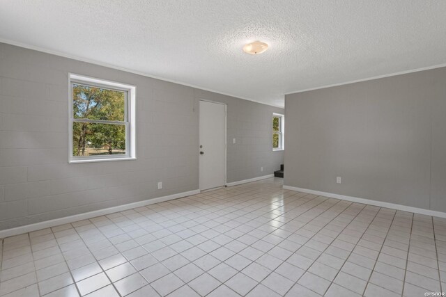 empty room featuring baseboards, ornamental molding, concrete block wall, and a healthy amount of sunlight