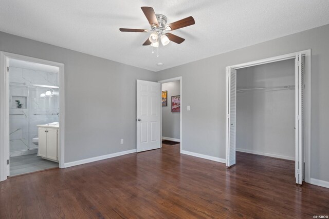 unfurnished bedroom featuring baseboards, dark wood finished floors, a ceiling fan, ensuite bathroom, and a closet