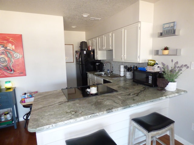 kitchen featuring a peninsula, white cabinetry, a kitchen breakfast bar, light stone countertops, and black appliances