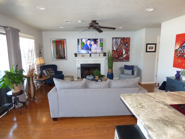 living area with a textured ceiling, visible vents, wood finished floors, and a tile fireplace