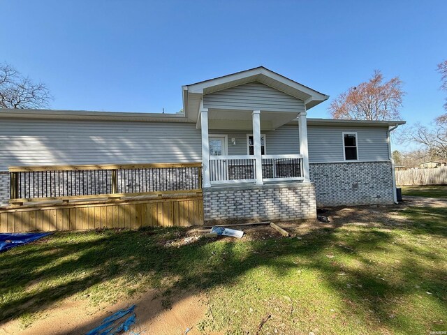 rear view of house featuring brick siding, a lawn, and fence