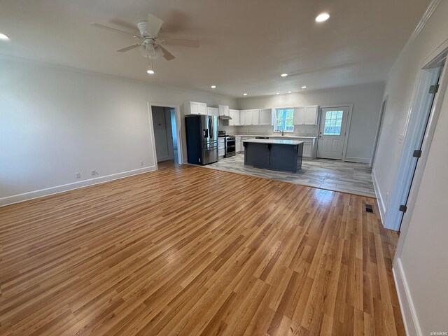 kitchen featuring stainless steel appliances, white cabinets, open floor plan, light countertops, and a center island