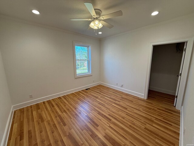 unfurnished bedroom featuring baseboards, light wood finished floors, a walk in closet, and crown molding