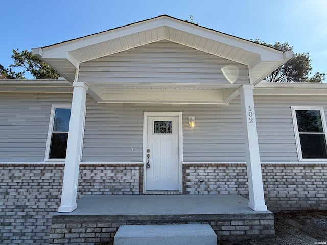 property entrance featuring covered porch and brick siding