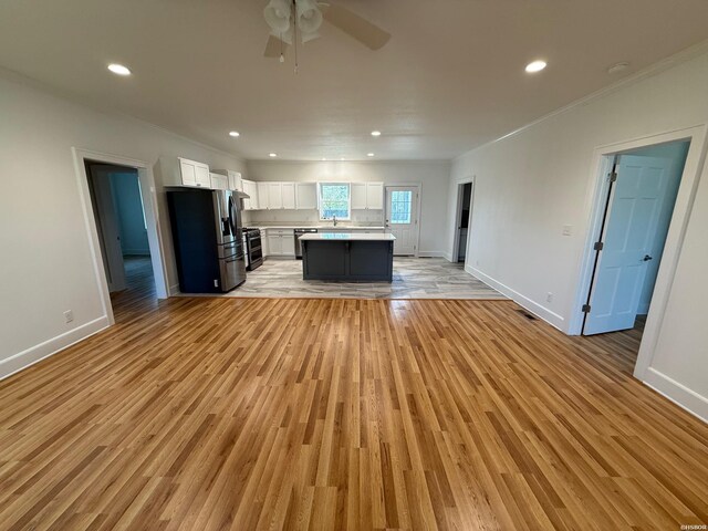 kitchen with open floor plan, a center island, stainless steel appliances, light countertops, and white cabinetry