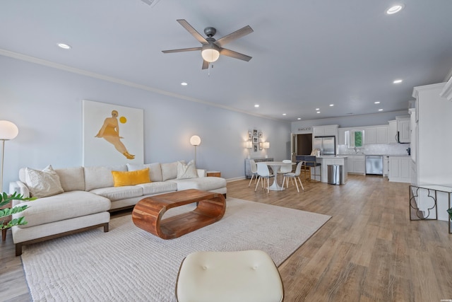 living room with crown molding, recessed lighting, a ceiling fan, baseboards, and light wood-type flooring