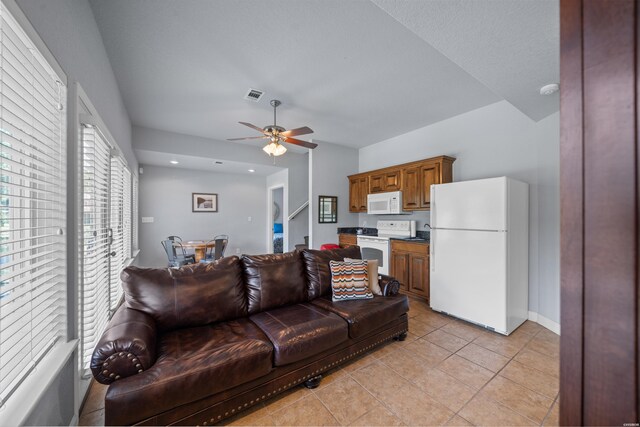 living area featuring light tile patterned flooring, ceiling fan, visible vents, and baseboards