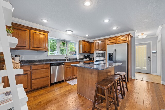 kitchen featuring a center island, brown cabinets, crown molding, a breakfast bar area, and appliances with stainless steel finishes