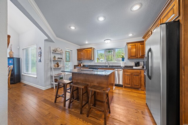 kitchen with a kitchen island, brown cabinets, stainless steel appliances, a kitchen bar, and a sink