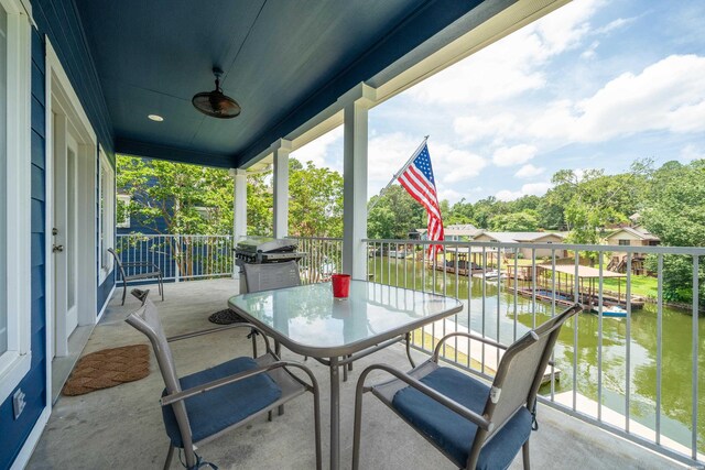 balcony featuring area for grilling, a boat dock, a water view, and a ceiling fan