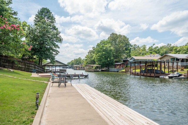 view of dock with a water view, a lawn, and fence