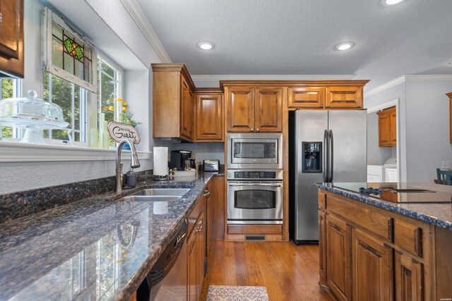 kitchen with light wood-style flooring, appliances with stainless steel finishes, dark stone countertops, crown molding, and a sink