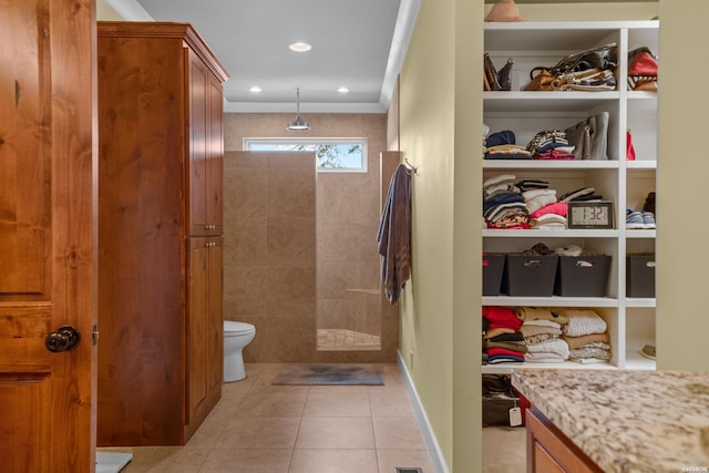 bathroom featuring a spacious closet, toilet, a tile shower, vanity, and tile patterned floors