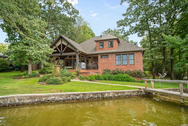 rear view of house featuring a yard, brick siding, a water view, and a shingled roof