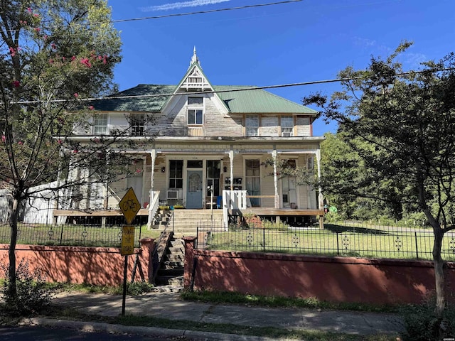 victorian home featuring metal roof, a porch, and a fenced front yard