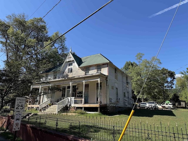 victorian home featuring a fenced front yard, covered porch, metal roof, and a front lawn