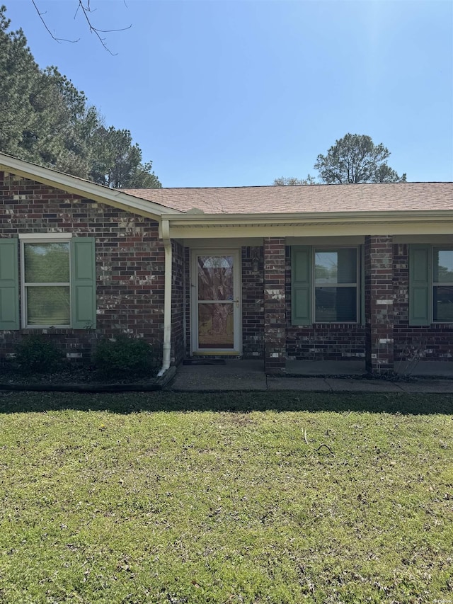 doorway to property with a yard, roof with shingles, and brick siding