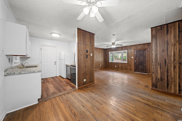 kitchen featuring wooden walls, electric range, dark wood-type flooring, white cabinets, and freestanding refrigerator