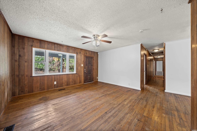 empty room with ceiling fan, wooden walls, visible vents, and dark wood finished floors