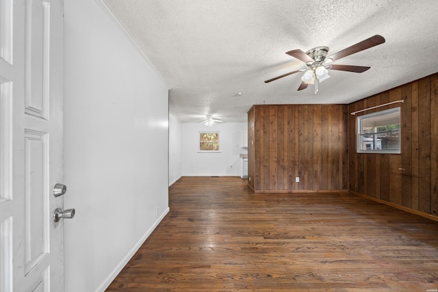 unfurnished room featuring a healthy amount of sunlight, ceiling fan, wooden walls, and dark wood-type flooring