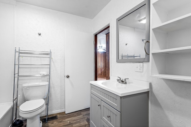 bathroom with a textured wall, vanity, toilet, and wood finished floors