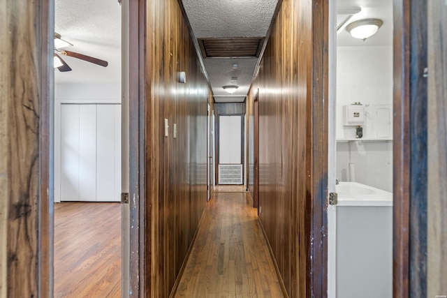 hall featuring a textured ceiling, wood finished floors, and wooden walls