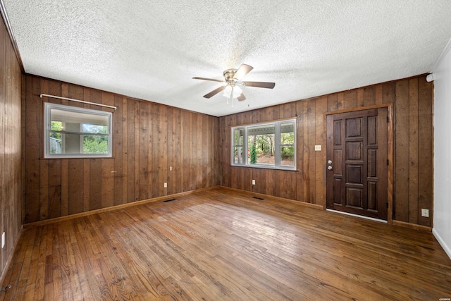 unfurnished room with baseboards, visible vents, ceiling fan, wood finished floors, and a textured ceiling