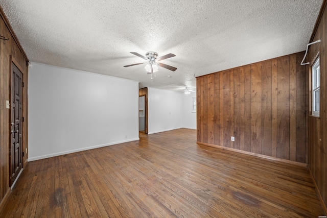 unfurnished room featuring wood walls, ceiling fan, a textured ceiling, and wood finished floors